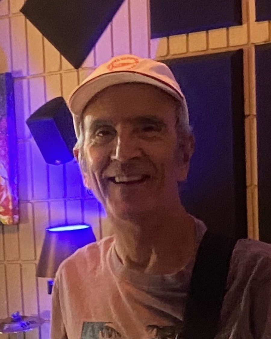 Barney Cortinez playing electric bass under stage lighting.